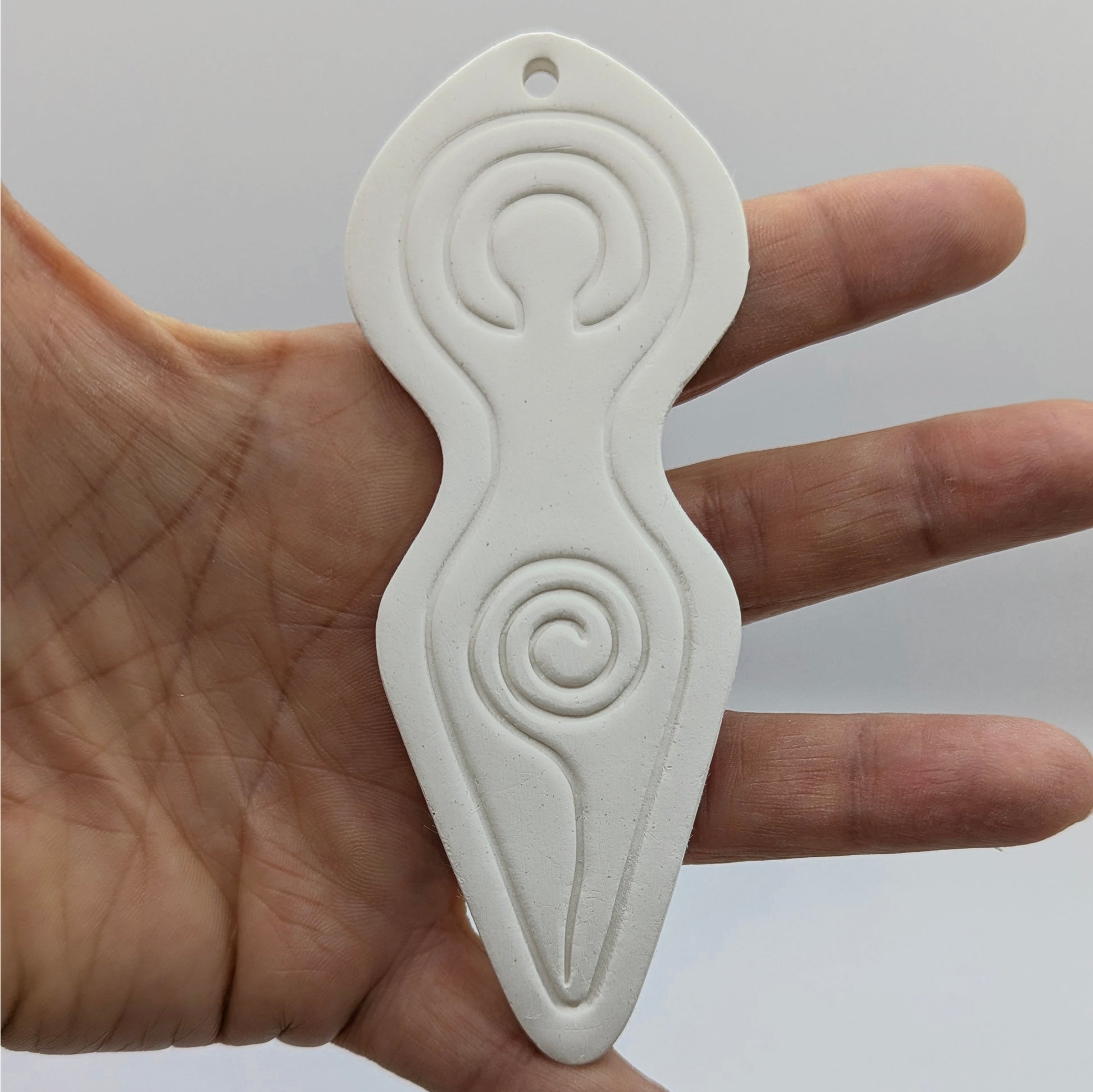 Spiral goddess shaped clay decoration shown on in some ones hand for scale
