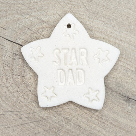 Star shaped white clay decoration / ornament with 'STAR DAD' text on a wooden surface