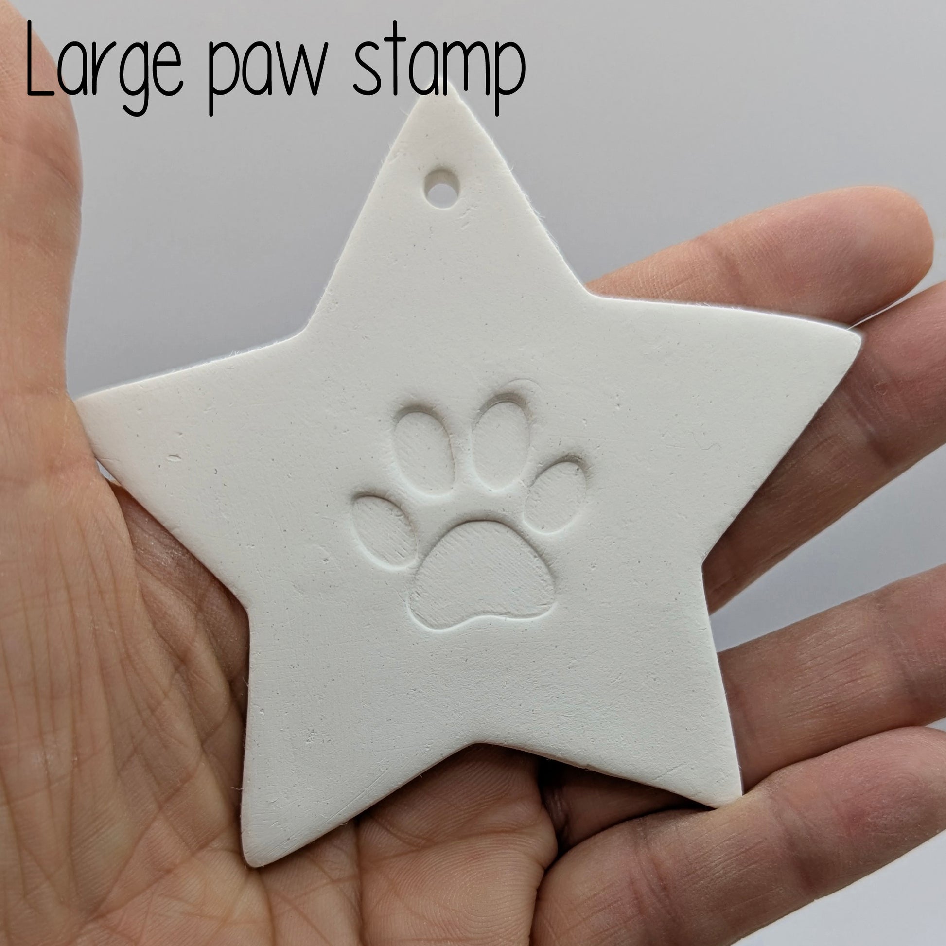 Star shaped clay decoration with a large paw print design in the centre held in some ones hand for scale