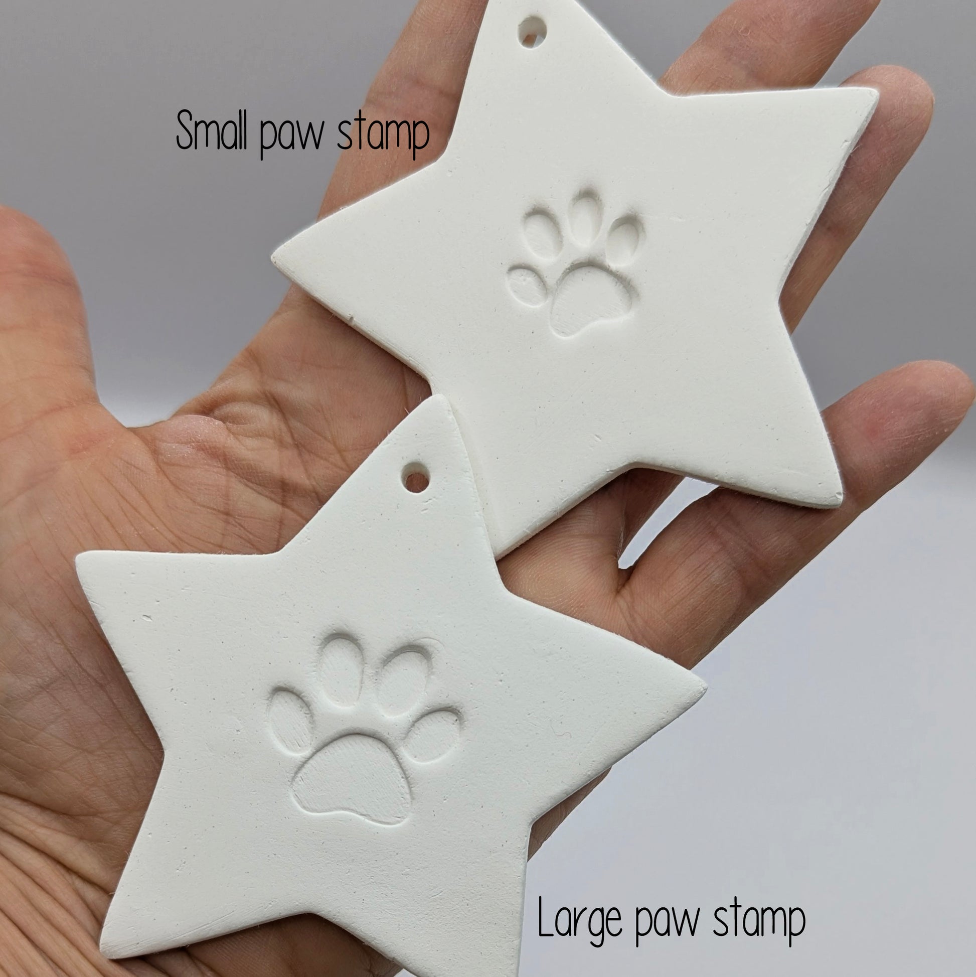two star shaped clay decoration with a paw print design in the centre of each star held in some ones hand for scale