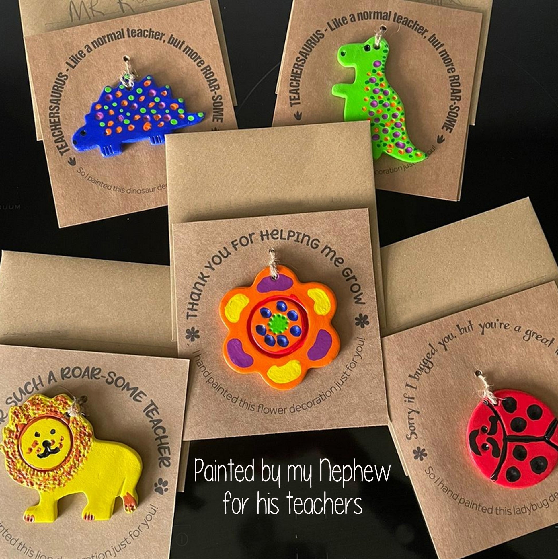 Colorful teacher thank you cards with a selection of clay decorations attached to the front of the kraft card, all painted in bright primary coloured paint