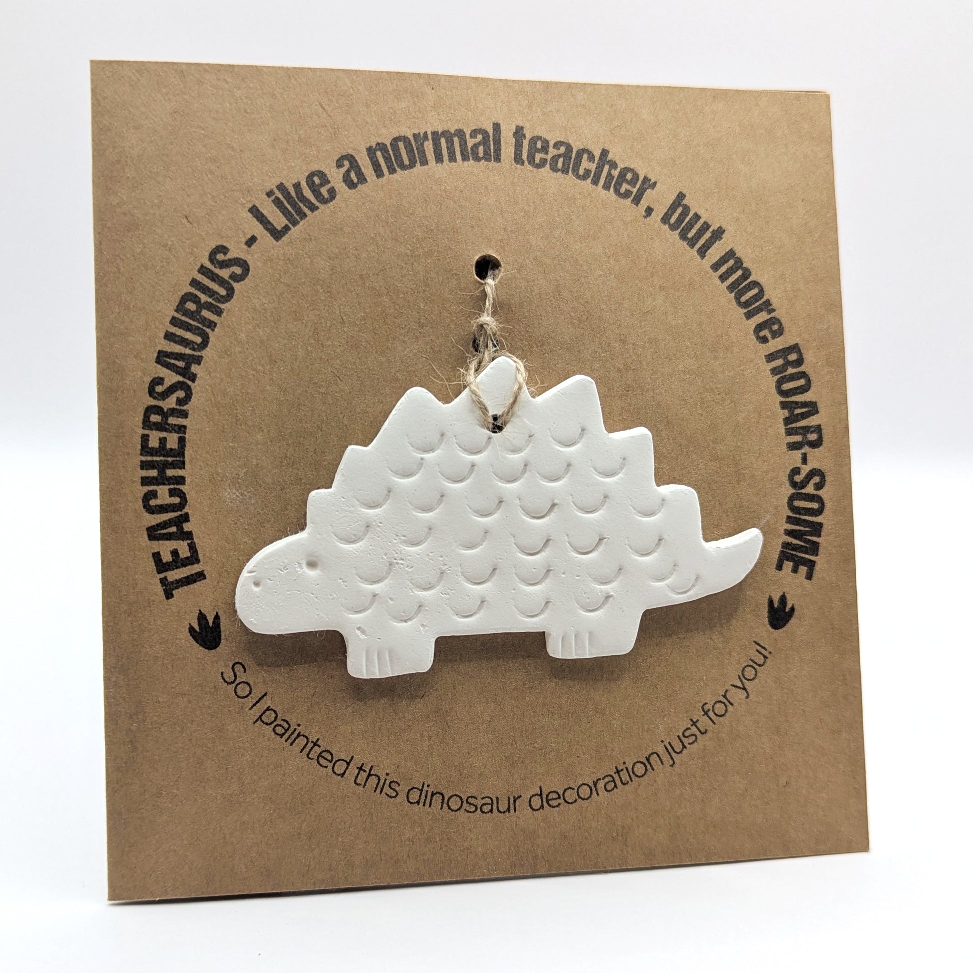 'Teachersaurus - like a normal teacher, but more roar-some' text on a brown kraft card with  a clay dinosaur decoration attached for you to paint and decorate