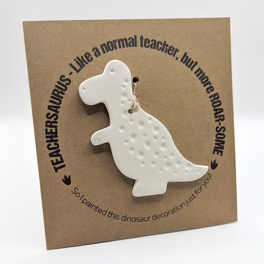 'Teachersaurus - like a normal teacher, but more roar-some' text on a brown kraft card with  a clay dinosaur decoration attached for you to paint and decorate