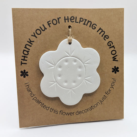'Thank you for helping me grow' text on a brown kraft card with  a clay flower decoration attached for you to paint and decorate
