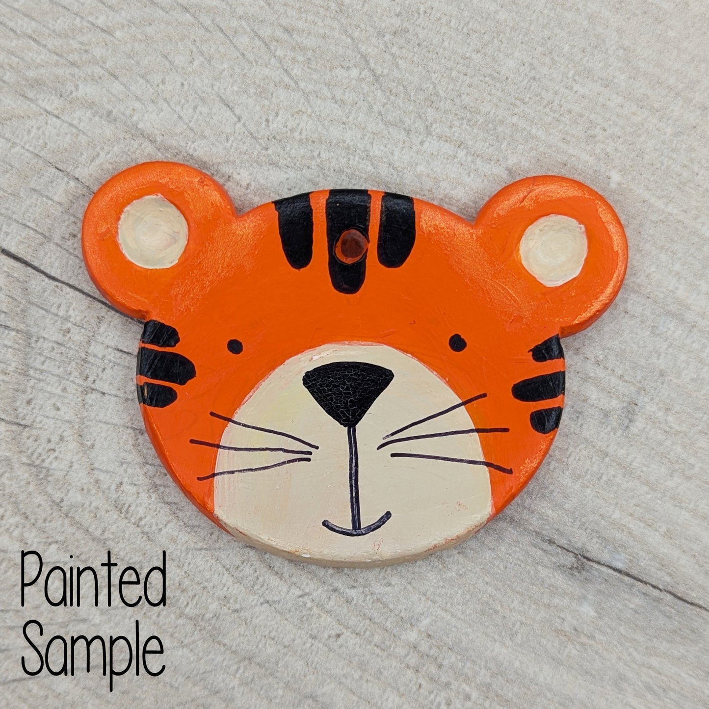 teddy bear face clay decoration painted to look like a tiger, orange with black stipes, cute nose and mouth