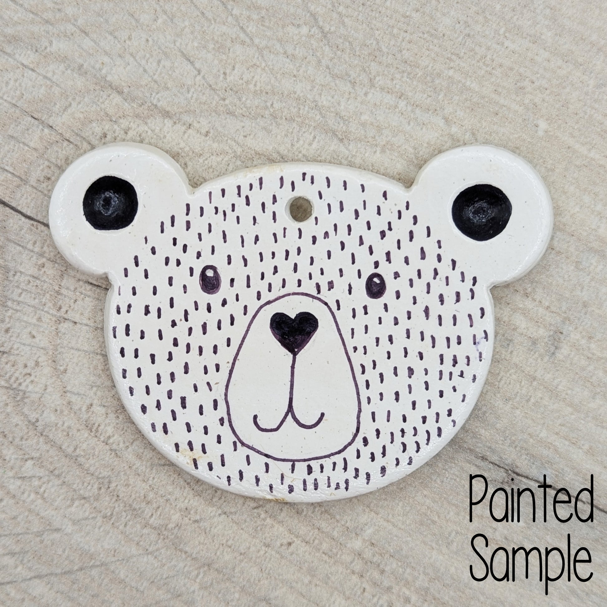 teddy bear face clay decoration, decorated in just black sharpie pen with a heart shaped nose and smiley mouth
