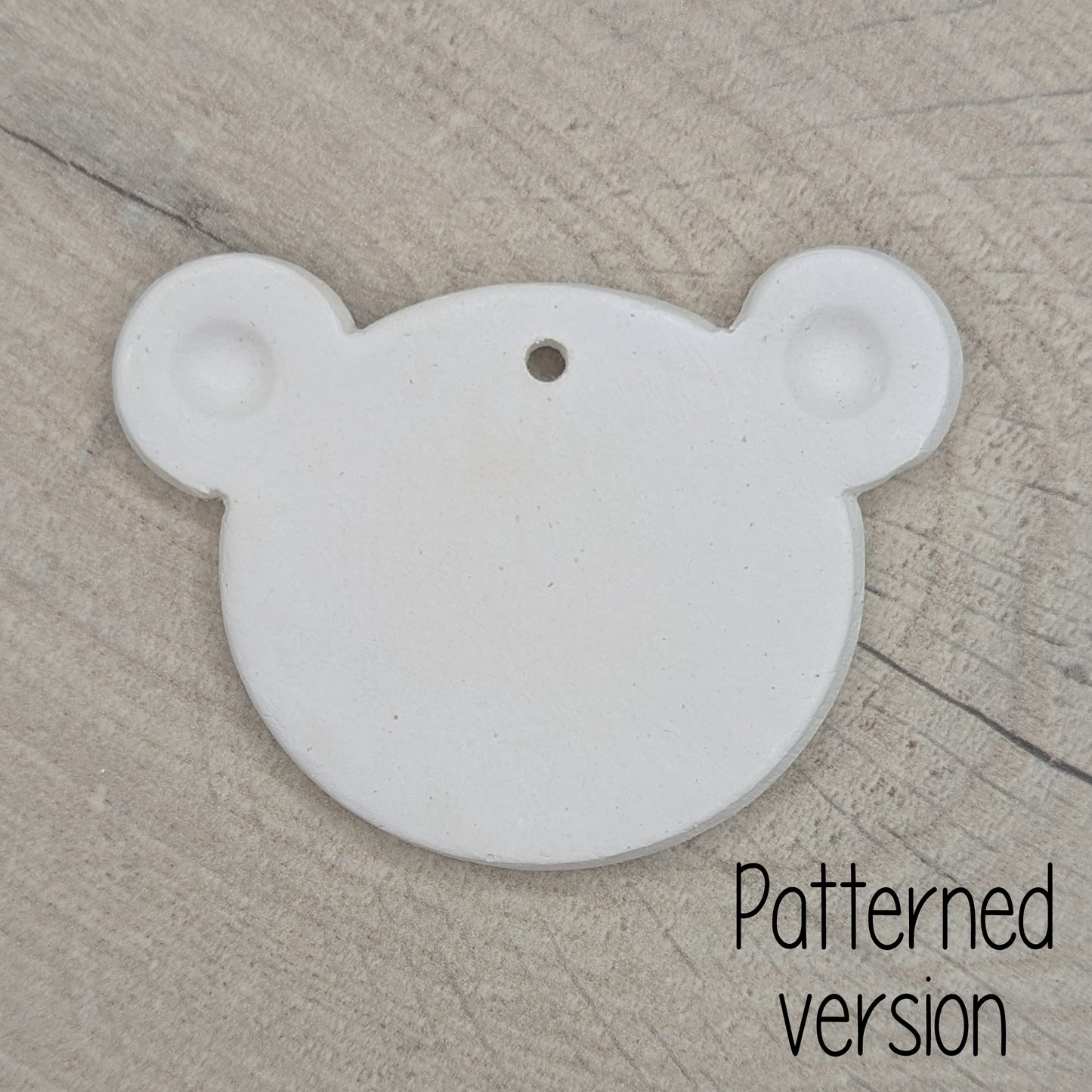 White clay decoration in the shape of a teddy bear head with ears stamped in on a wooden surface