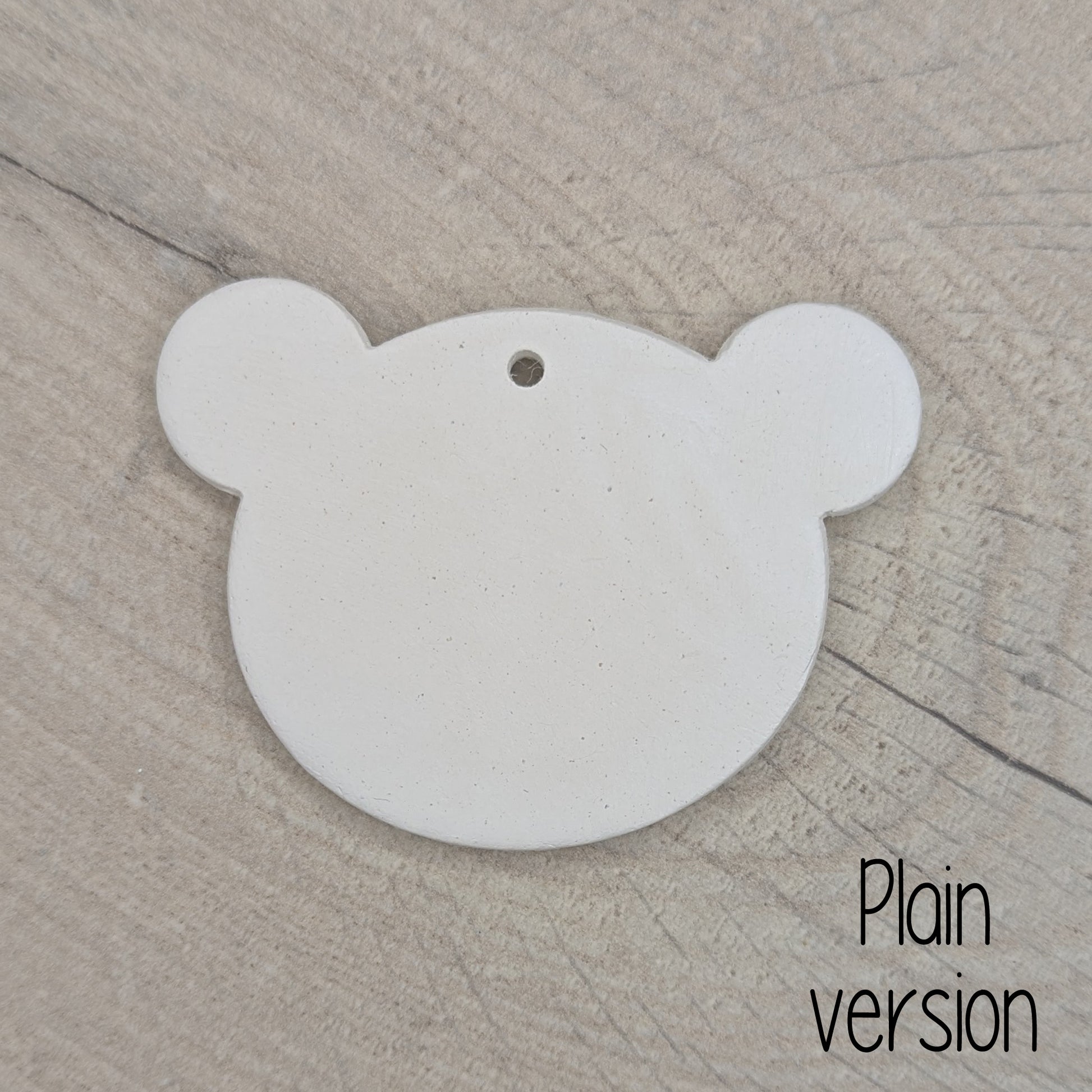 White clay decoration in the shape of a teddy bear head, on a wooden surface