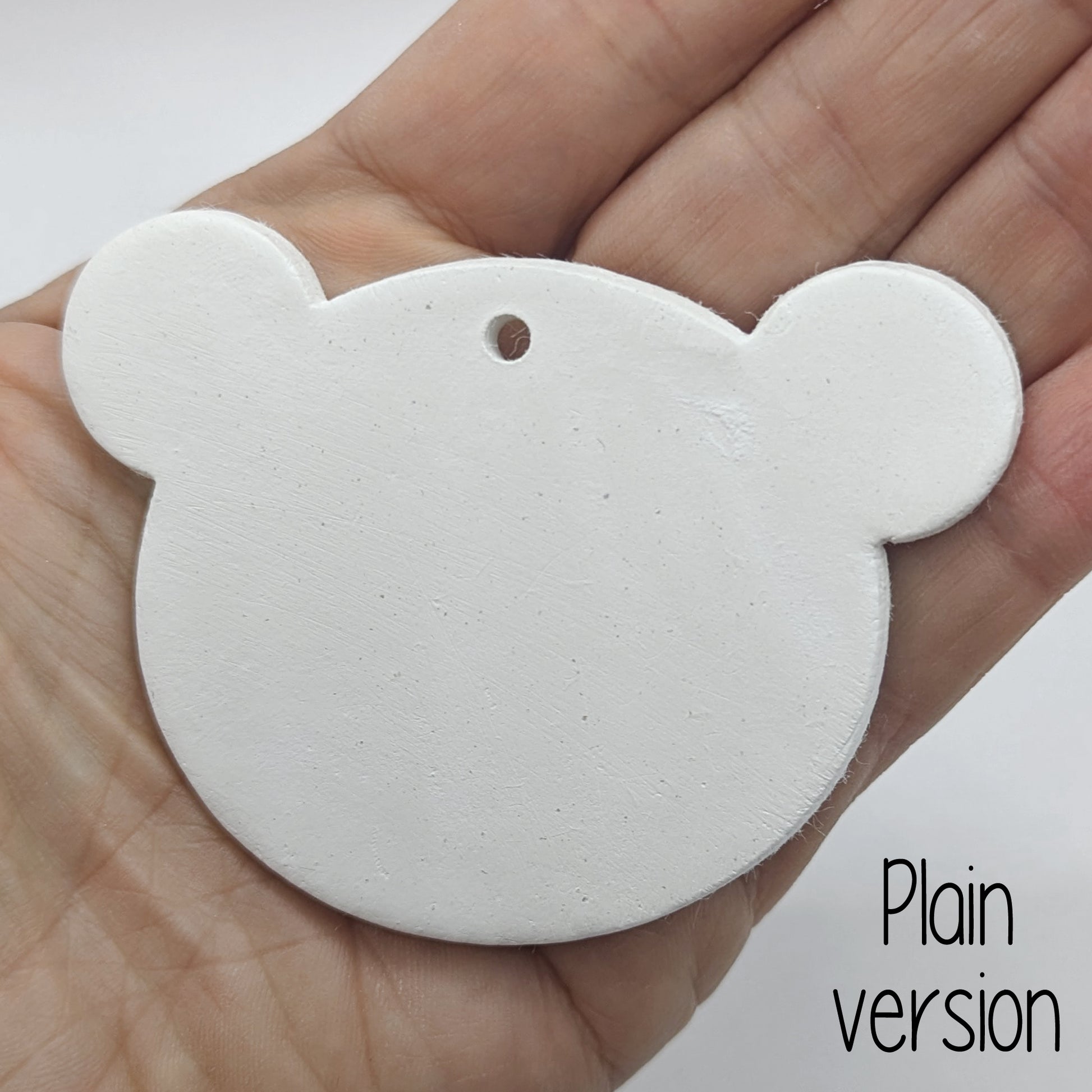 White clay decoration in the shape of a teddy bear head held in hand for scale