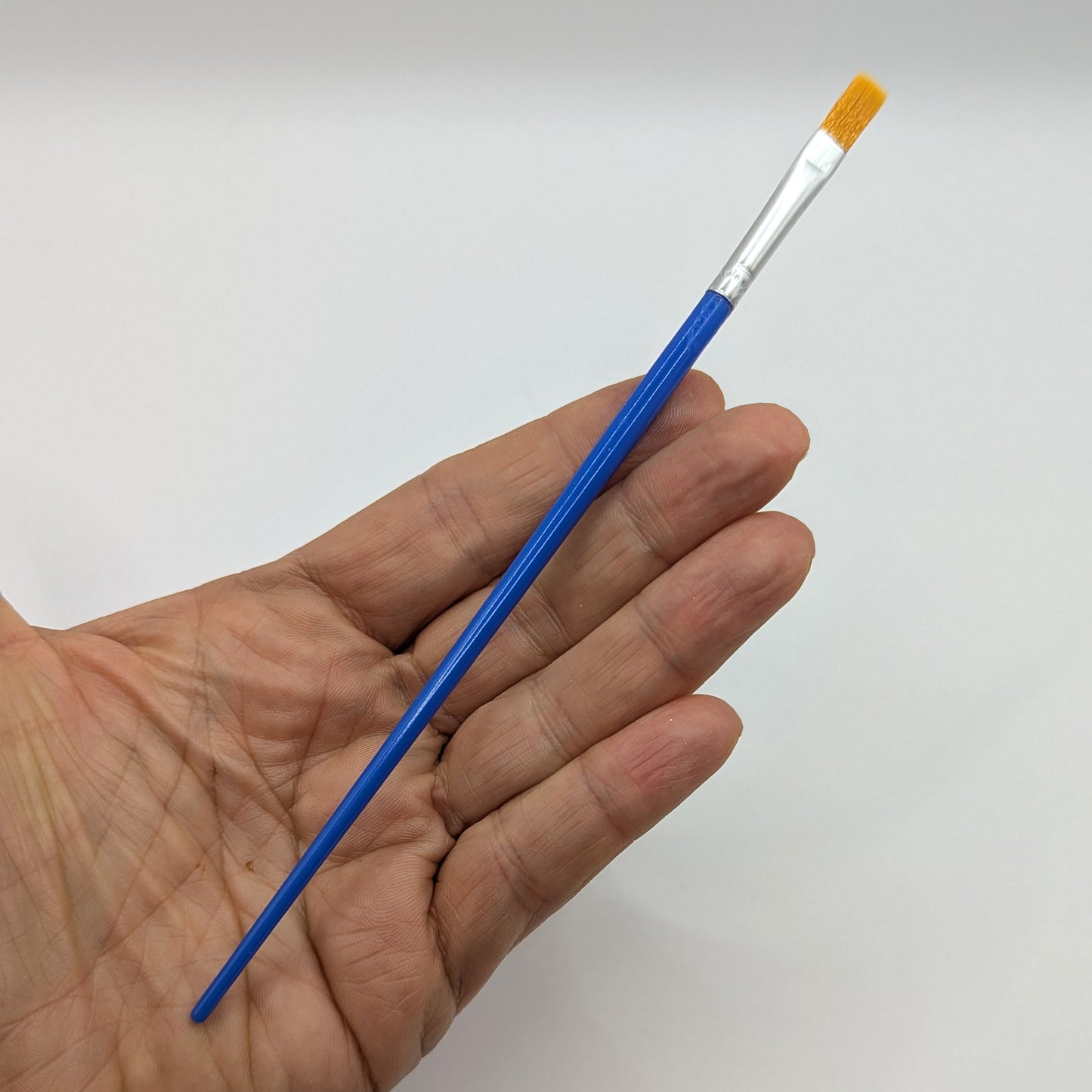 Hand holding a blue wide tip paintbrush 