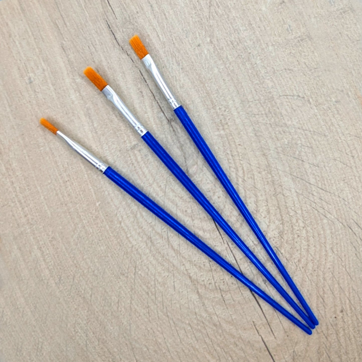 Three wide tip paintbrushes with blue handles and orange bristles 