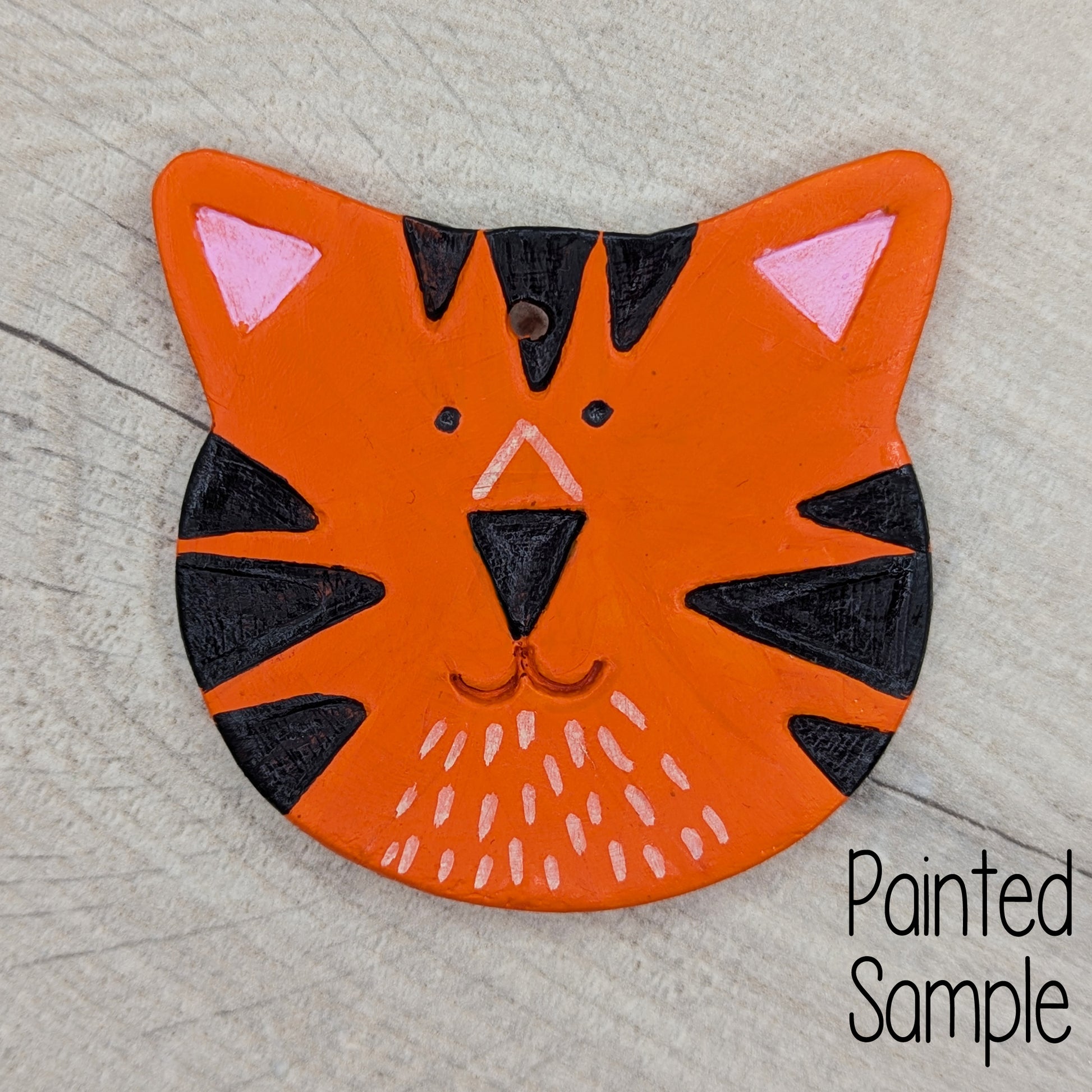 Tiger head shaped clay decoration, painted in orange with black tiger stripes