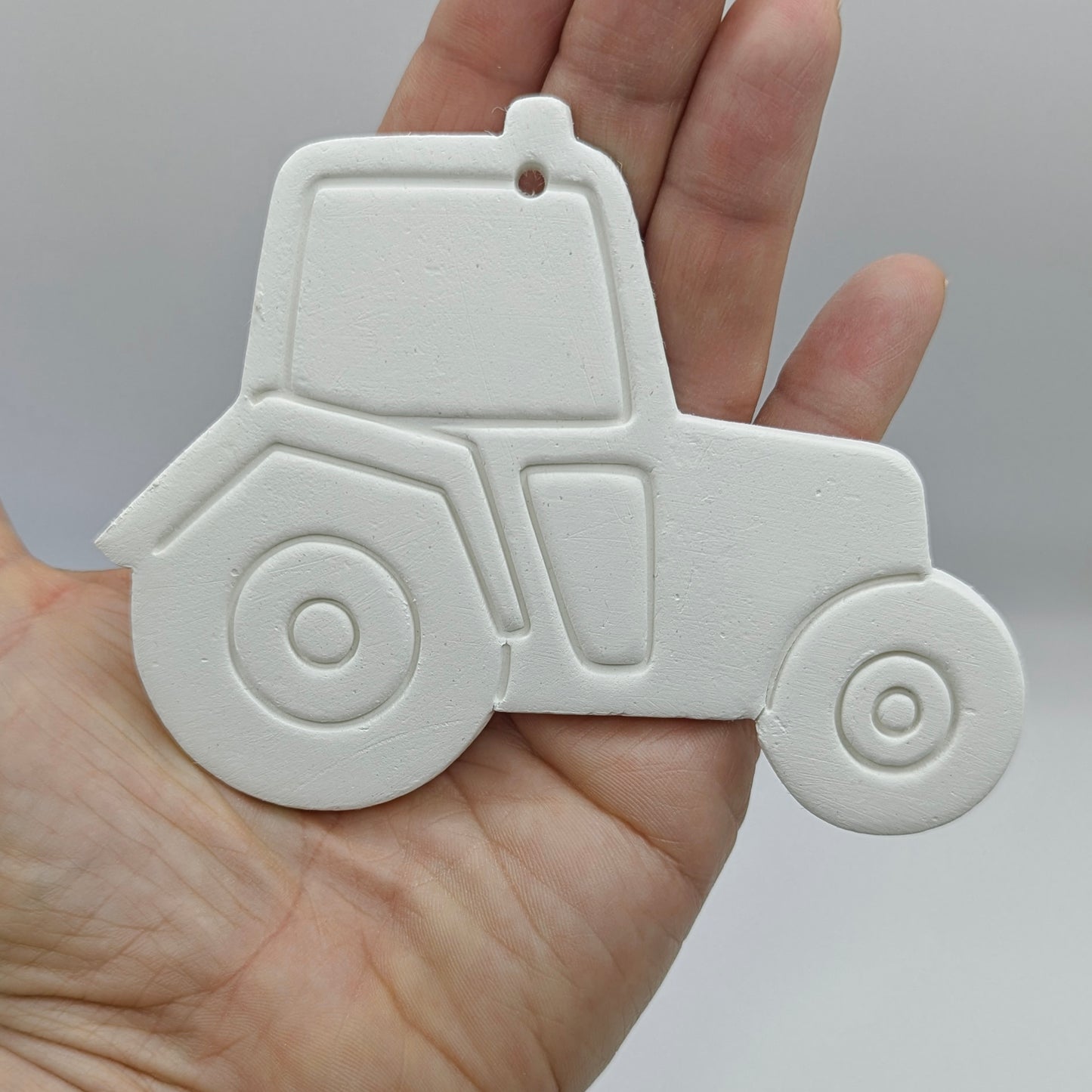 White clay tractor ornament held in a hand against a gray background