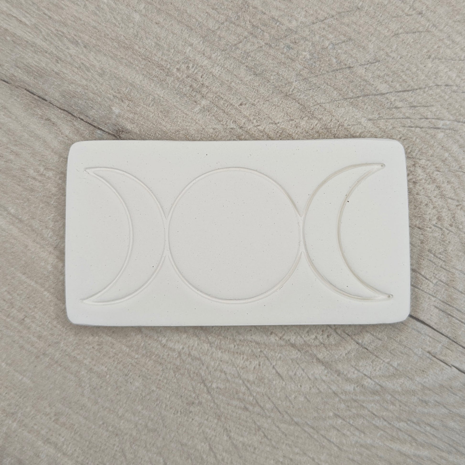 rectangular shaped air dried clay decoration with the triple moon symbol stamped into it on a wooden background