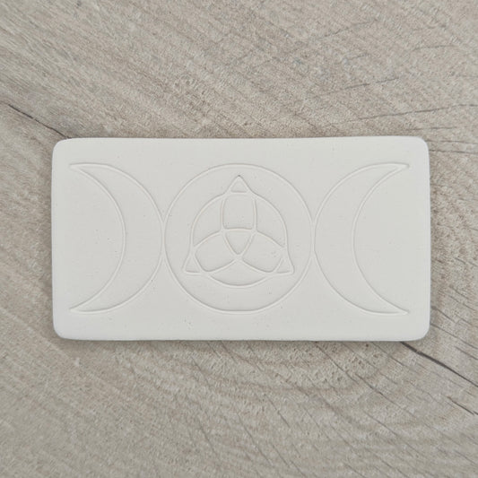 rectangular shaped air dried clay decoration with the triple moon and triquetra symbols stamped into it on a wooden background