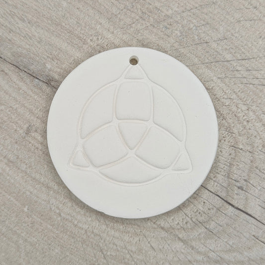 white air dried clay decoration with the triquetra symbol stamped into it on a wooden background