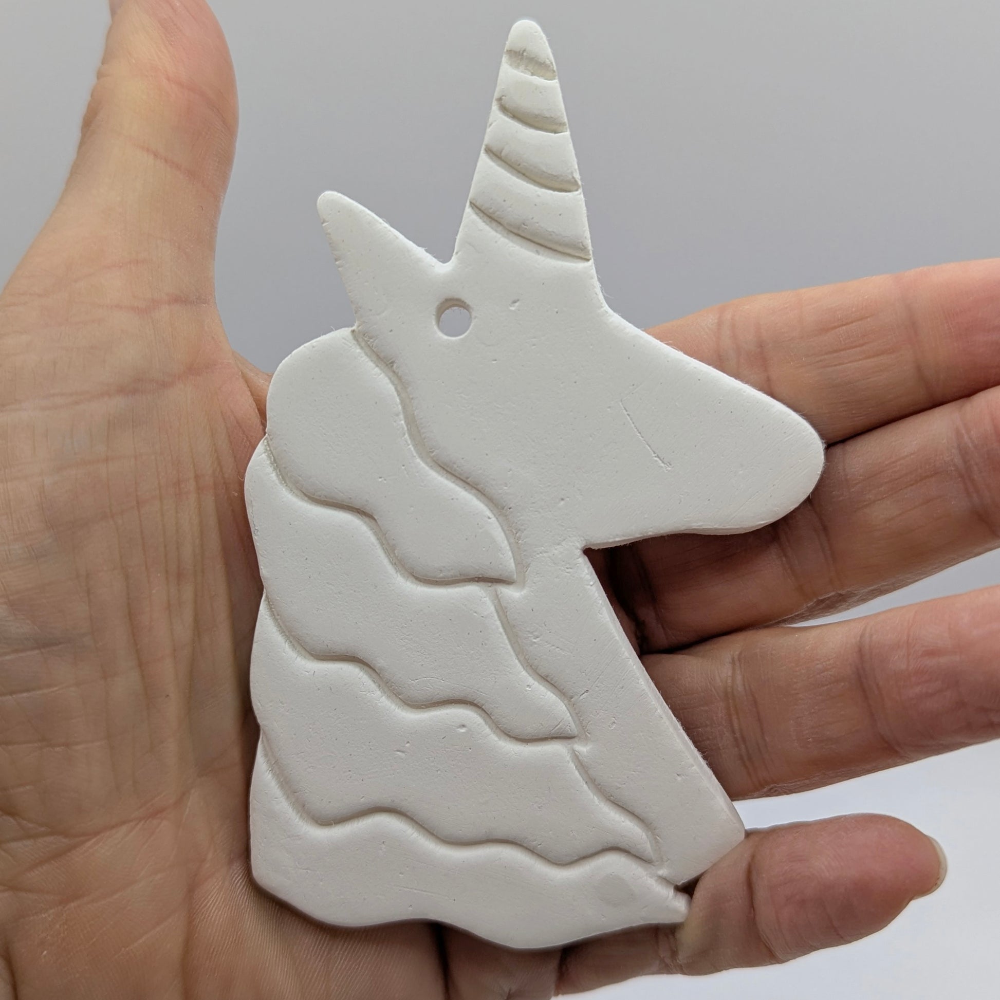 hand holding a unicorn clay decoration to show scale