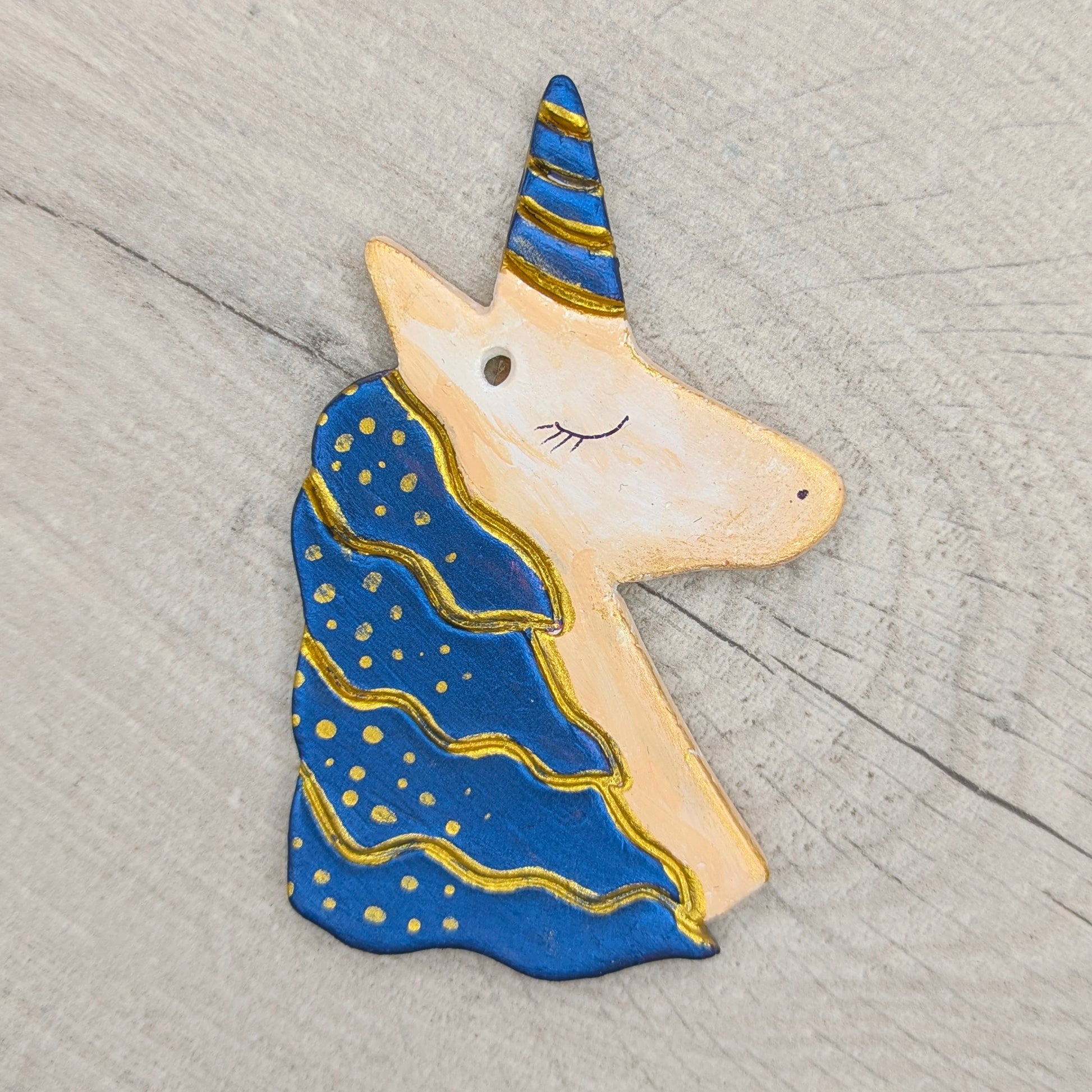 Unicorn-shaped clay decoration painted in blue and gold on a wooden surface