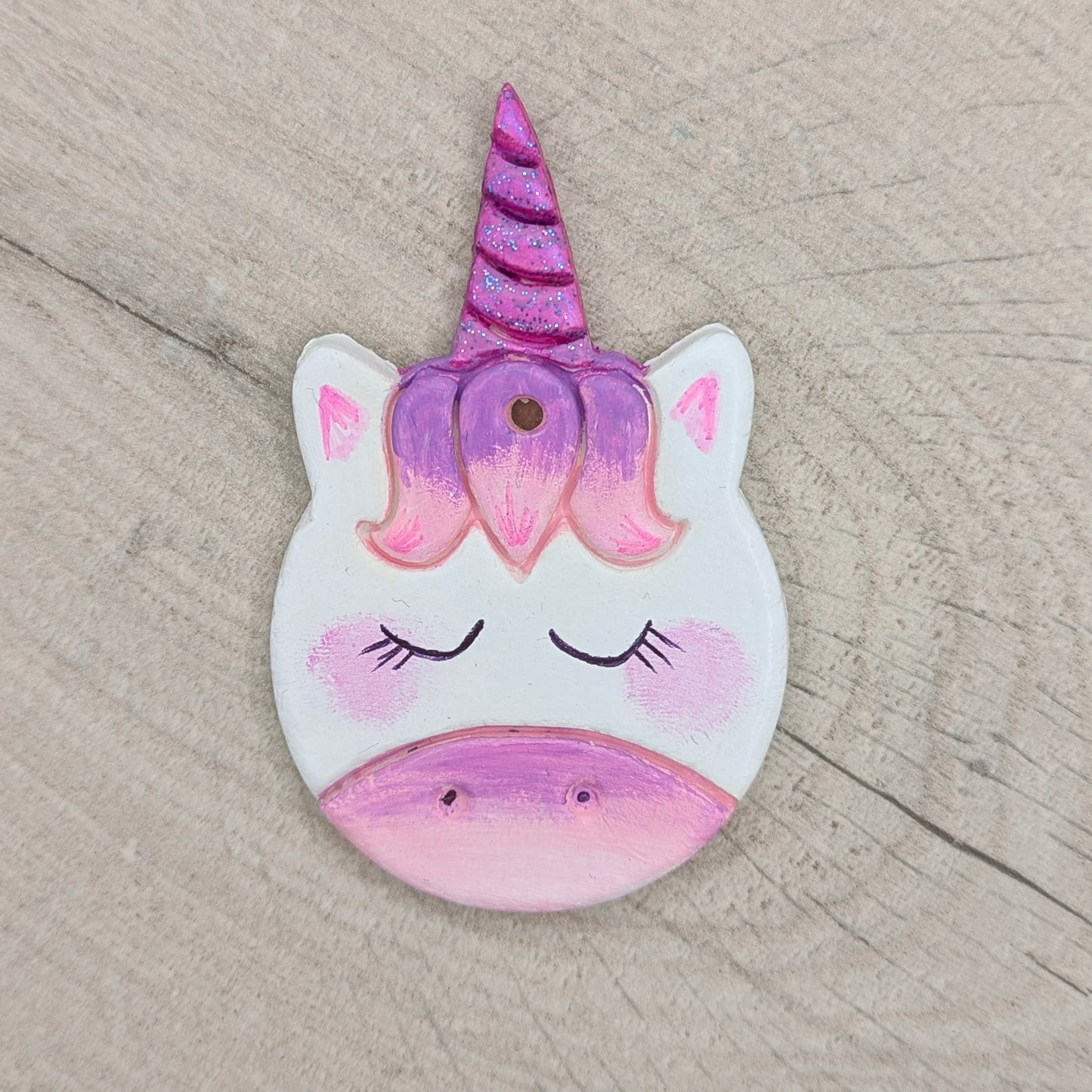 Unicorn-shaped decoration with a purple horn and pink face on a wooden surface