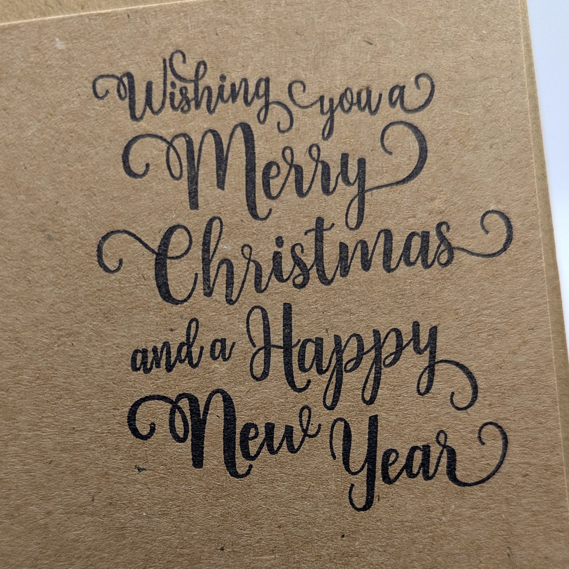 close up of wishing you a merry Christmas and a happy new year, stamped in black ink onto a kraft card