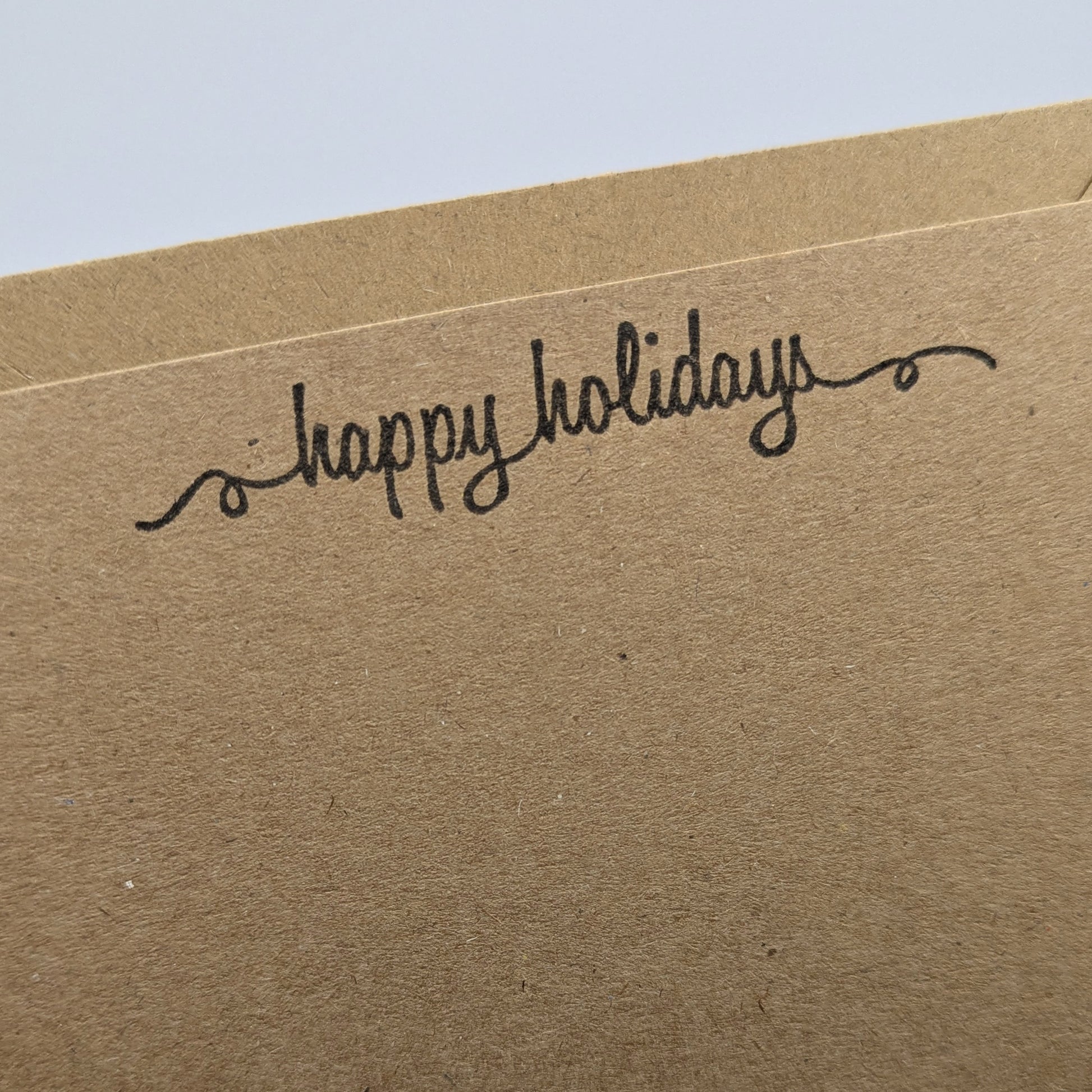 happy holidays stamped in black ink onto a kraft card