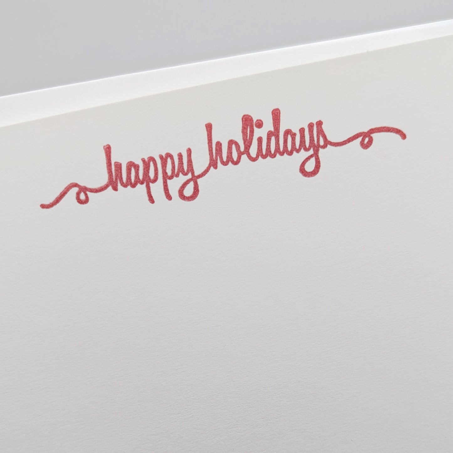 close up of happy holidays stamped in red ink onto a white card