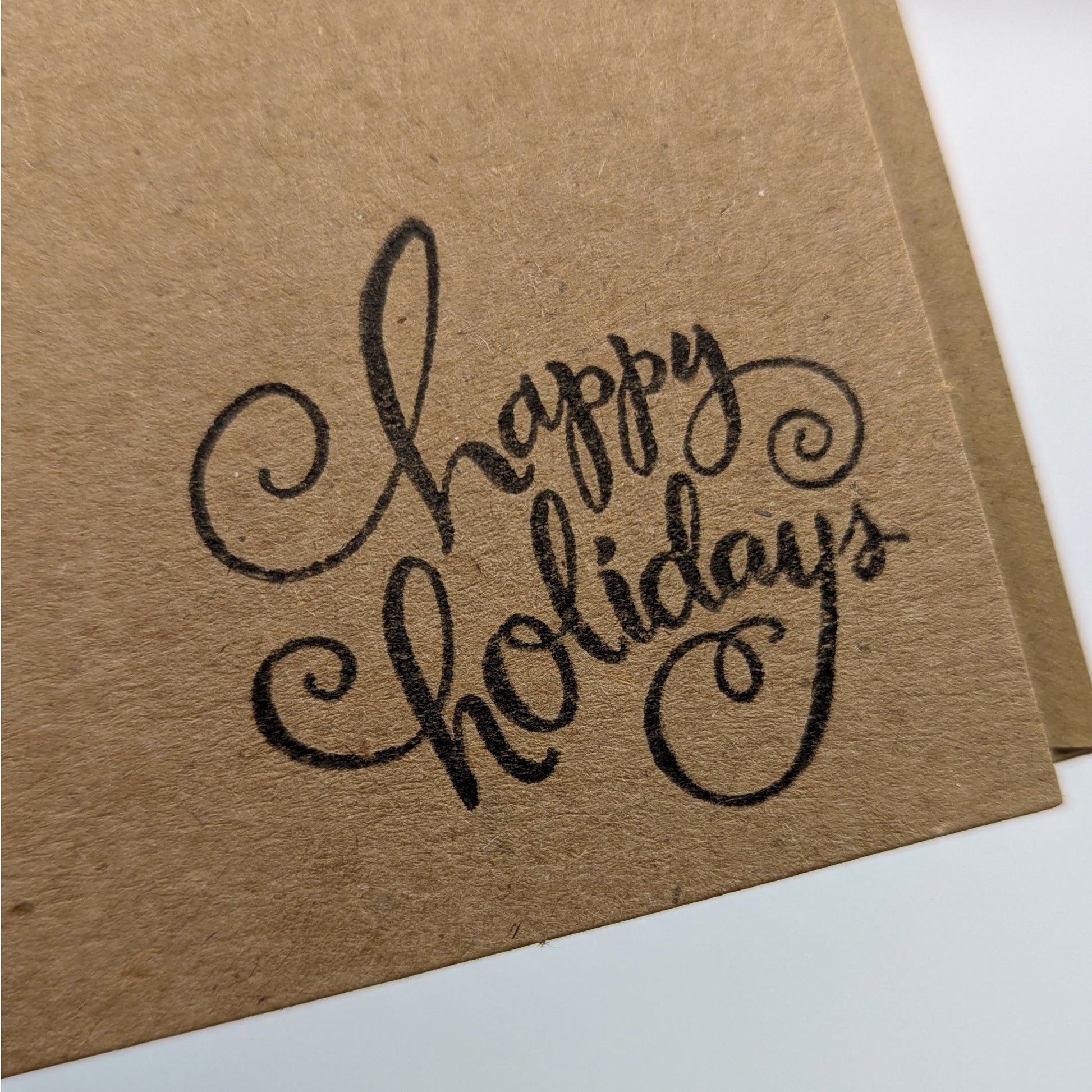 close up of happy holidays stamped in black ink onto a kraft card, 