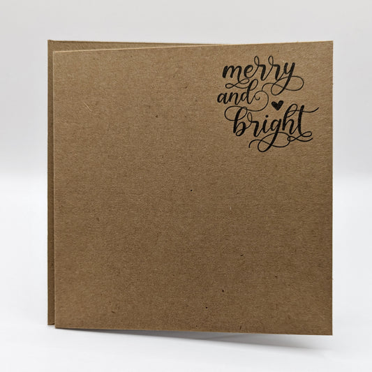 close up of wording 'merry and bright' in a script font, stamped in black ink onto a kraft card comes with matching envelope