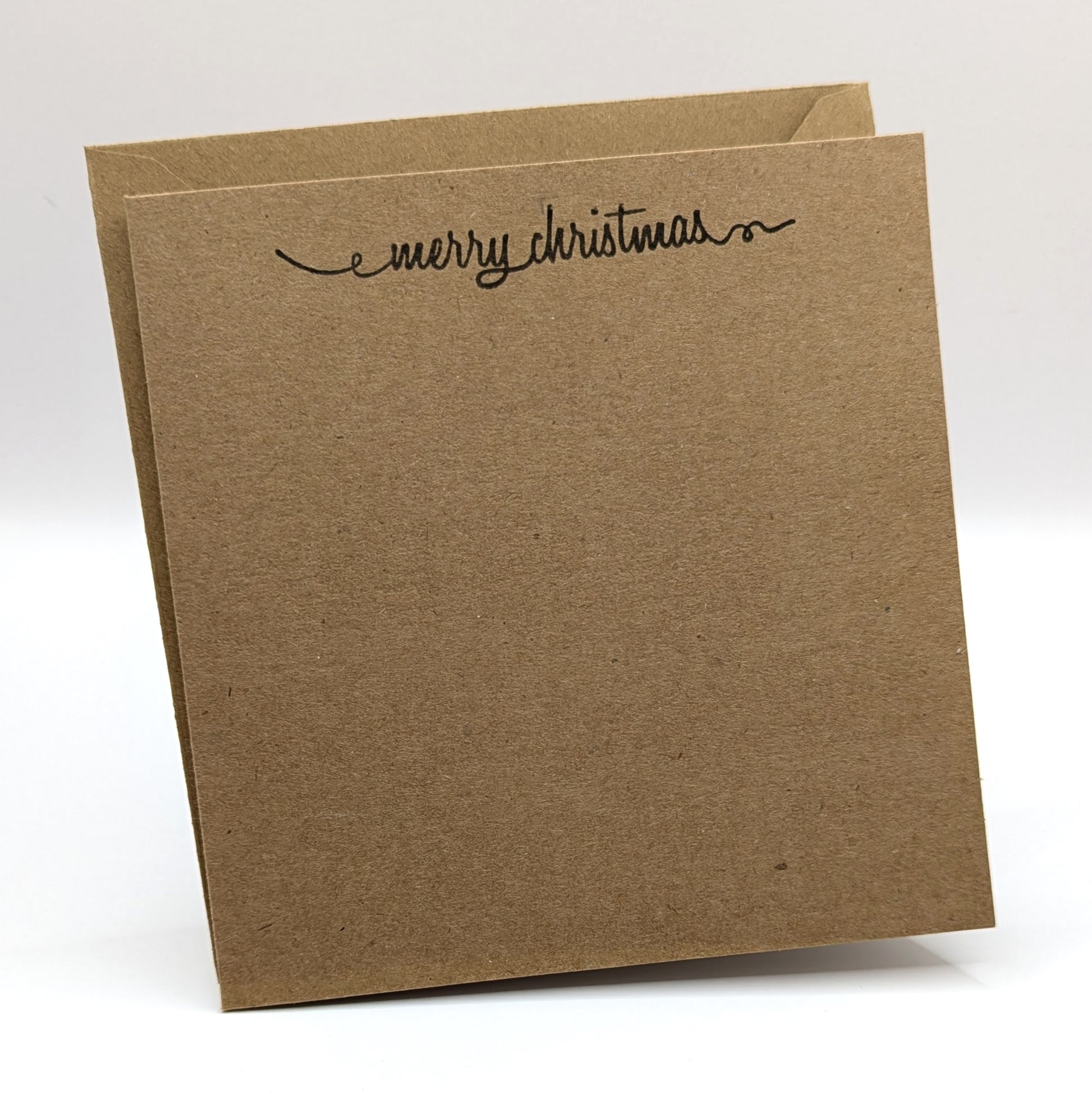 merry Christmas in a script font, stamped in black ink onto a kraft card comes with matching envelope