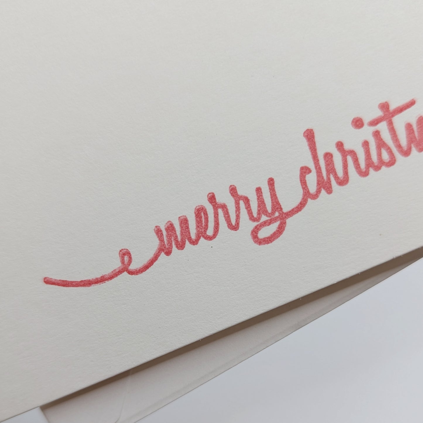 close up of merry Christmas in a script font, stamped in red ink onto a white card comes