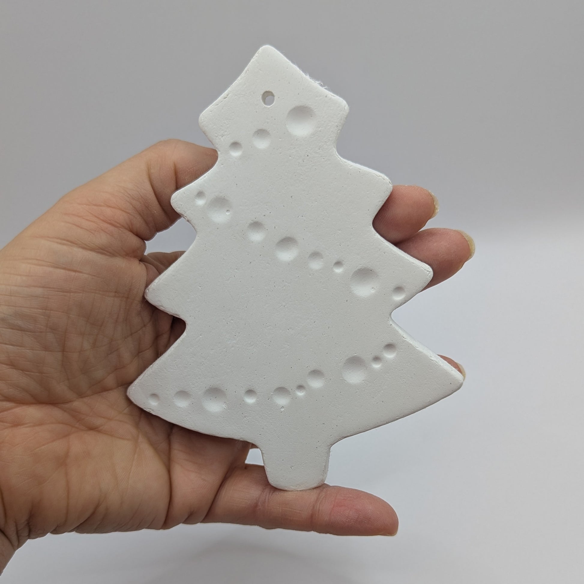 white air dried clay Christmas tree decoration held in hand with tinsel pattern stamped into the clay